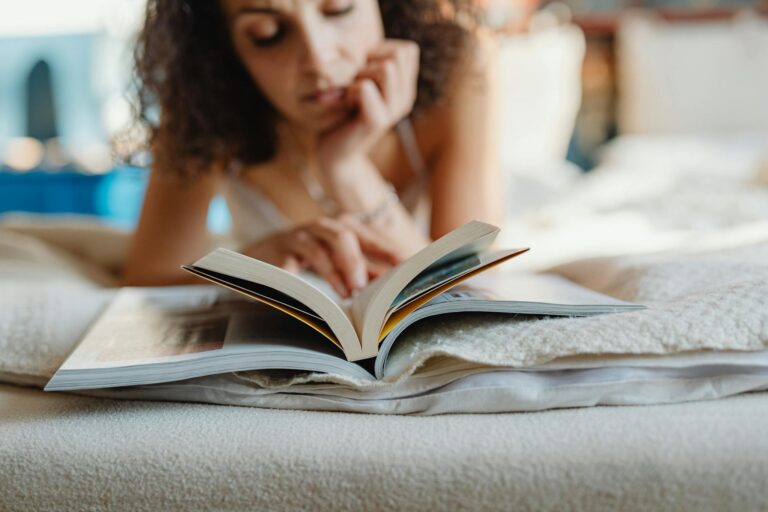 A woman with curly hair relaxes while reading a book indoors. Perfect for relaxation and leisure themes.