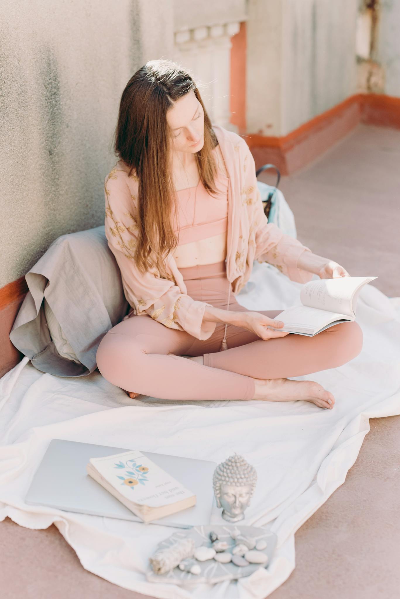 A young woman in activewear meditatively reading outside, surrounded by a peaceful setting.